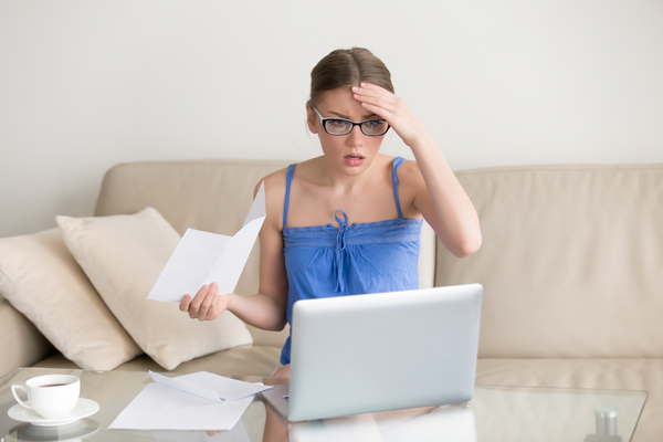 A stressed person sitting at a table with bills, a laptop, and a bank card, symbolizing financial fatigue and money-related stress.