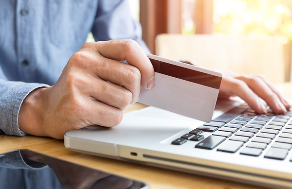 Osoba trzyma kartę bankową i korzysta z laptopa, wykonując płatność online.